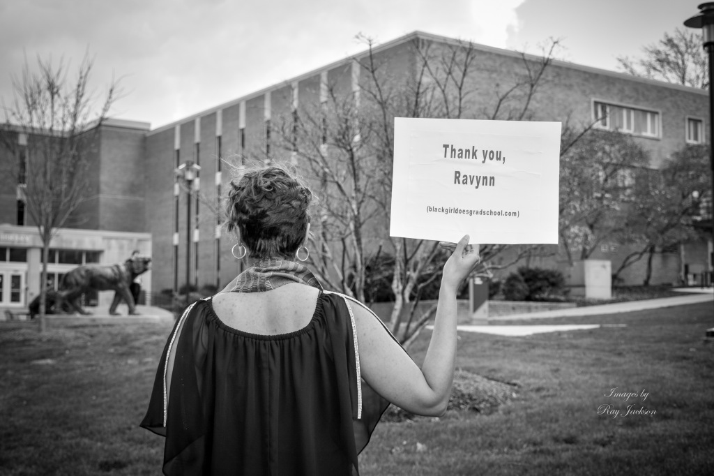A black and white photo of the blogger holding a sign saying "Thank you, Ravynn" with the Black Girl Does Grad School website blackgirldoesgradschool.com